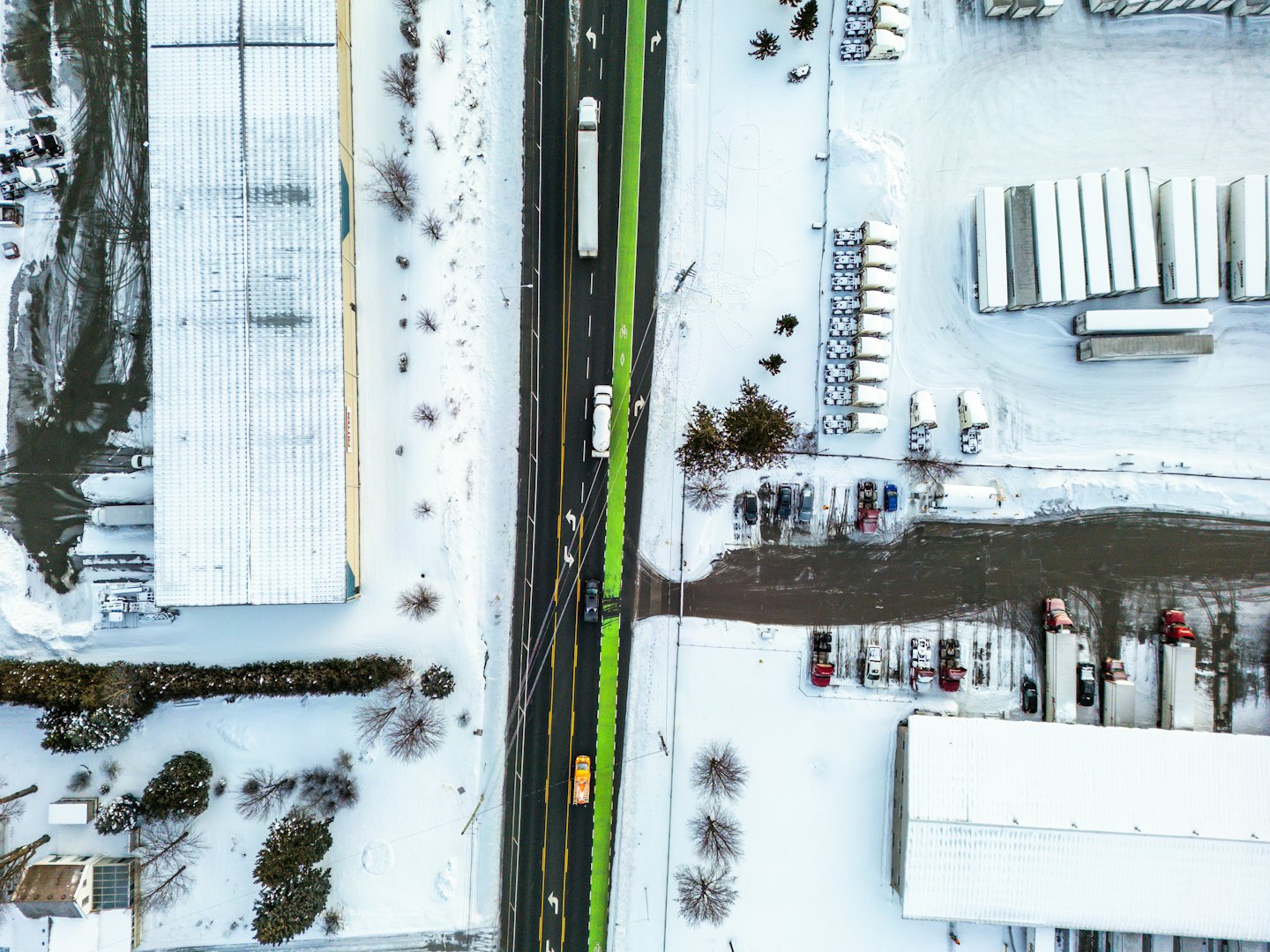 Schneebedeckter Industriekomplex mit Autos auf einer Straße.