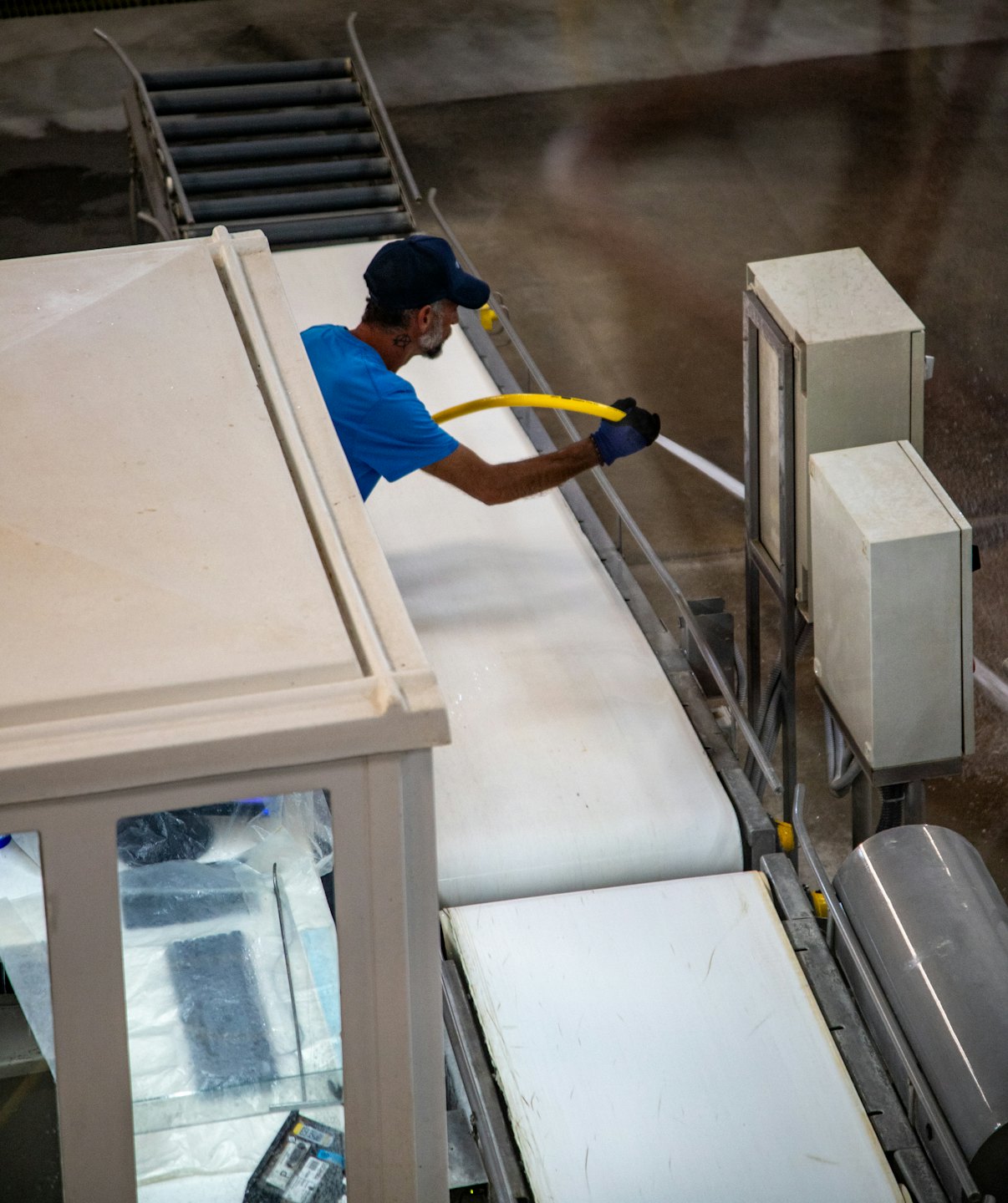 Arbeiter in blauer Kappe reinigt industrielles Förderband.
