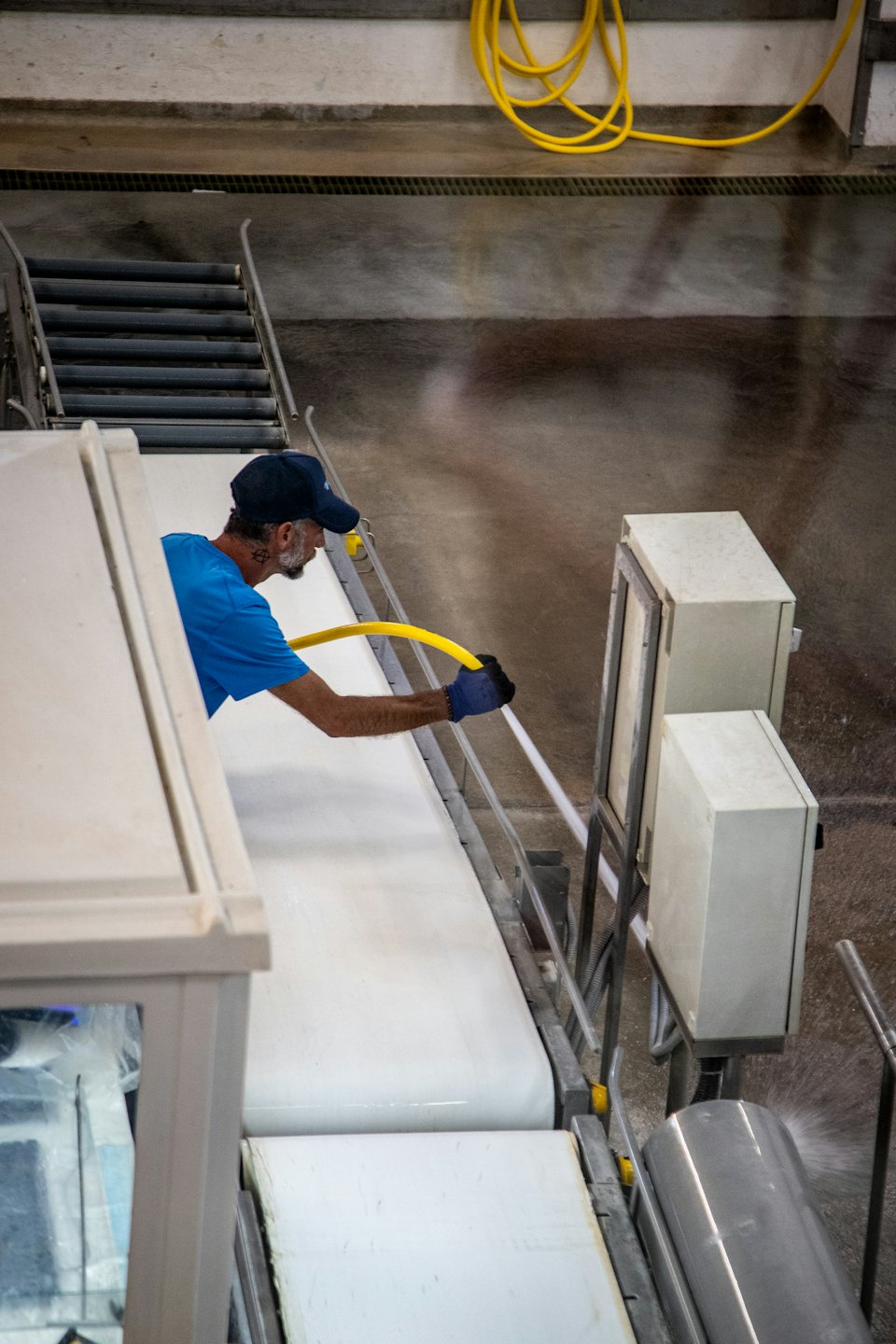 Arbeiter in blauem Hemd reinigt Industriemaschinen mit einem Schlauch.